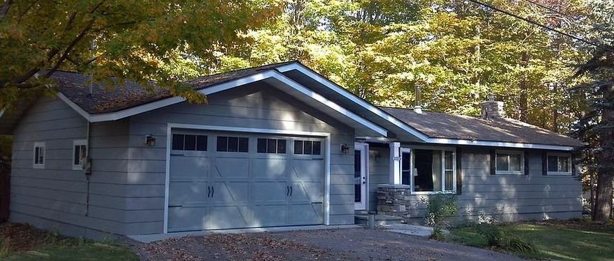 Suburban gray house with attached garage, white trim, and trees in the front yard