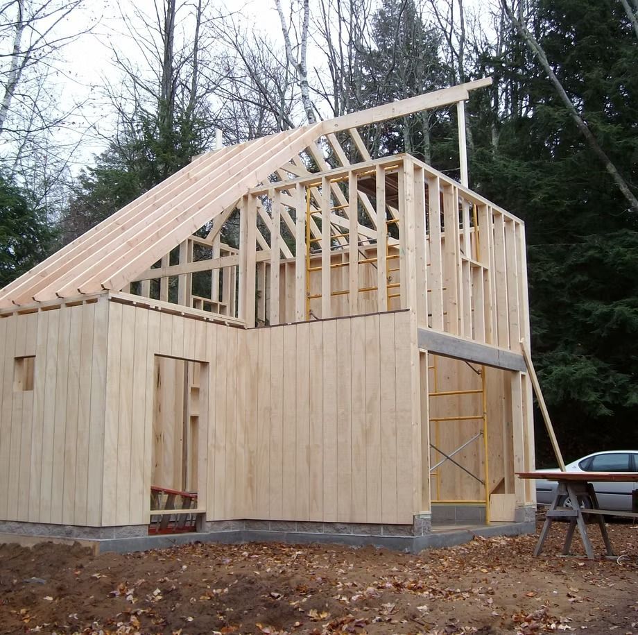 Partially framed wooden house under construction with exposed roof trusses and unfinished walls