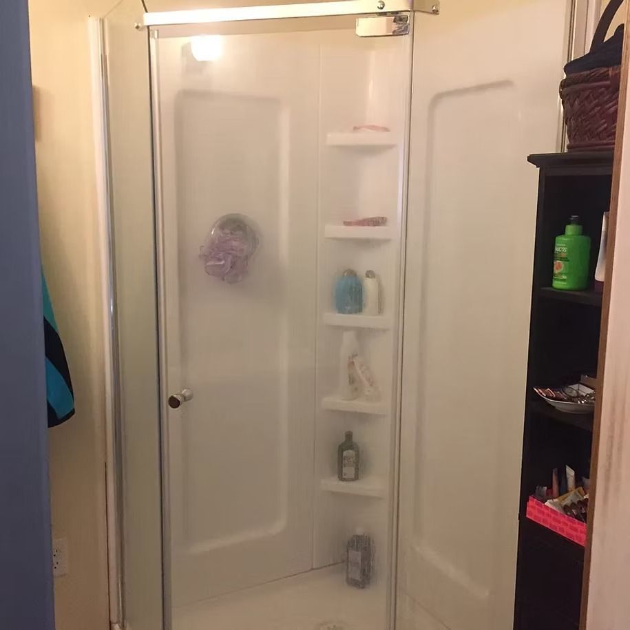 Bathroom with a glass shower door and built-in corner shelves holding toiletries