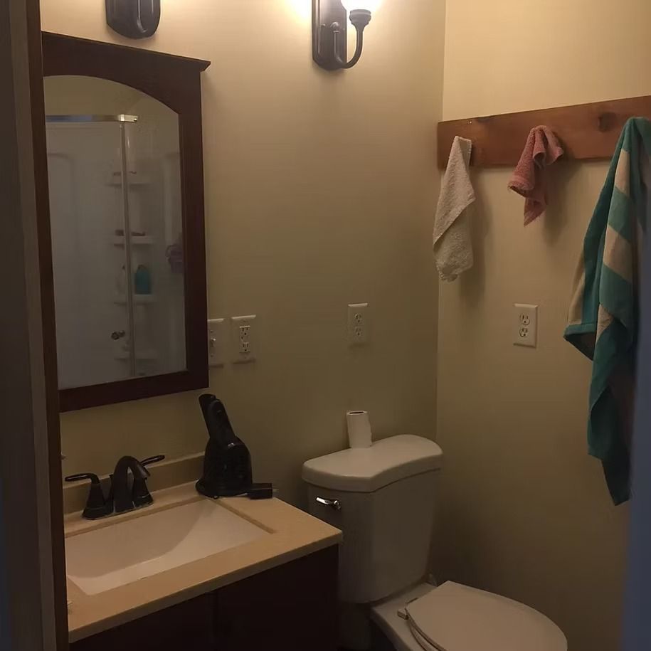 Small bathroom with vanity, mirror, toilet, wall hooks, and towels hanging on the right.