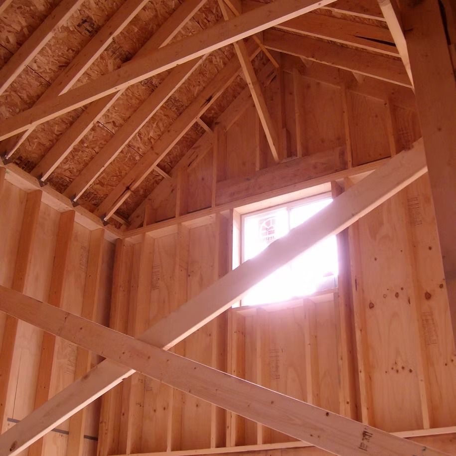 Interior of a wooden shed with exposed beams and a small sunlit window.