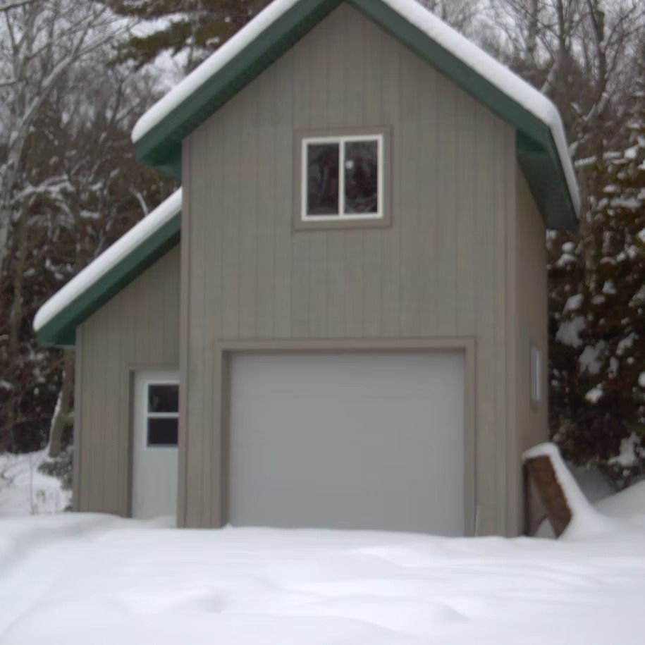 Snow-covered garage with beige siding and green roof trim in a winter yard