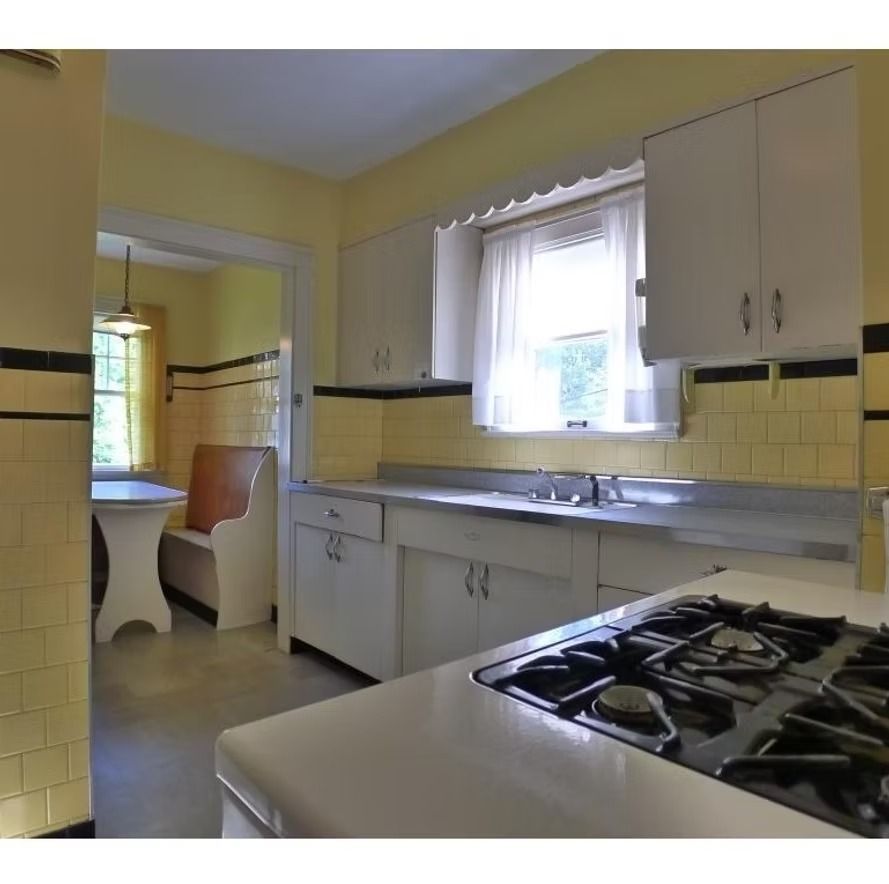 Yellow vintage kitchen with white cabinets, sink under a window, and a gas stove in the foreground