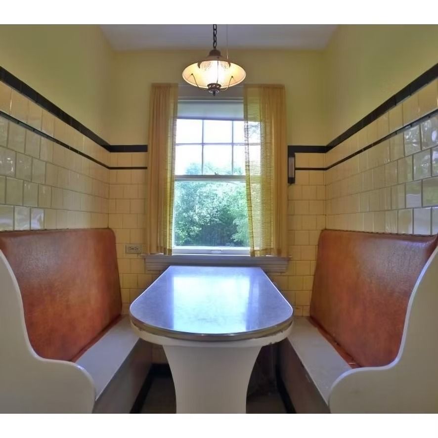 Retro diner booth with cream tile walls, brown seats, and a table by a window