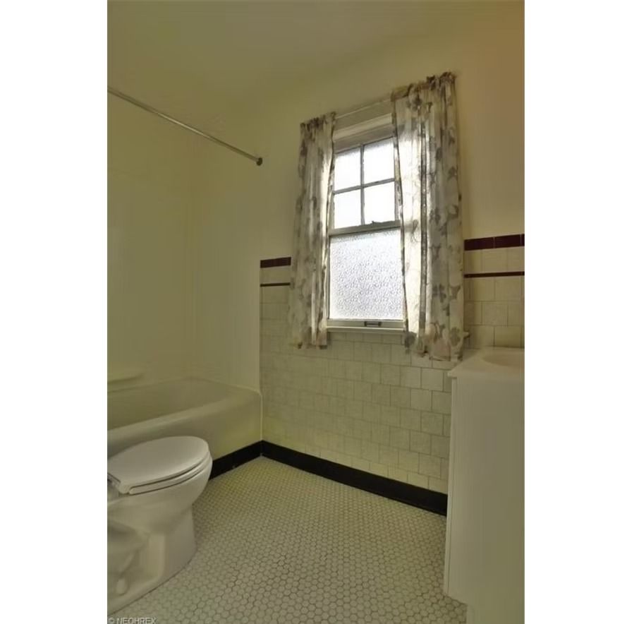 Small vintage bathroom with toilet, pedestal sink, and frosted window with sheer curtains.