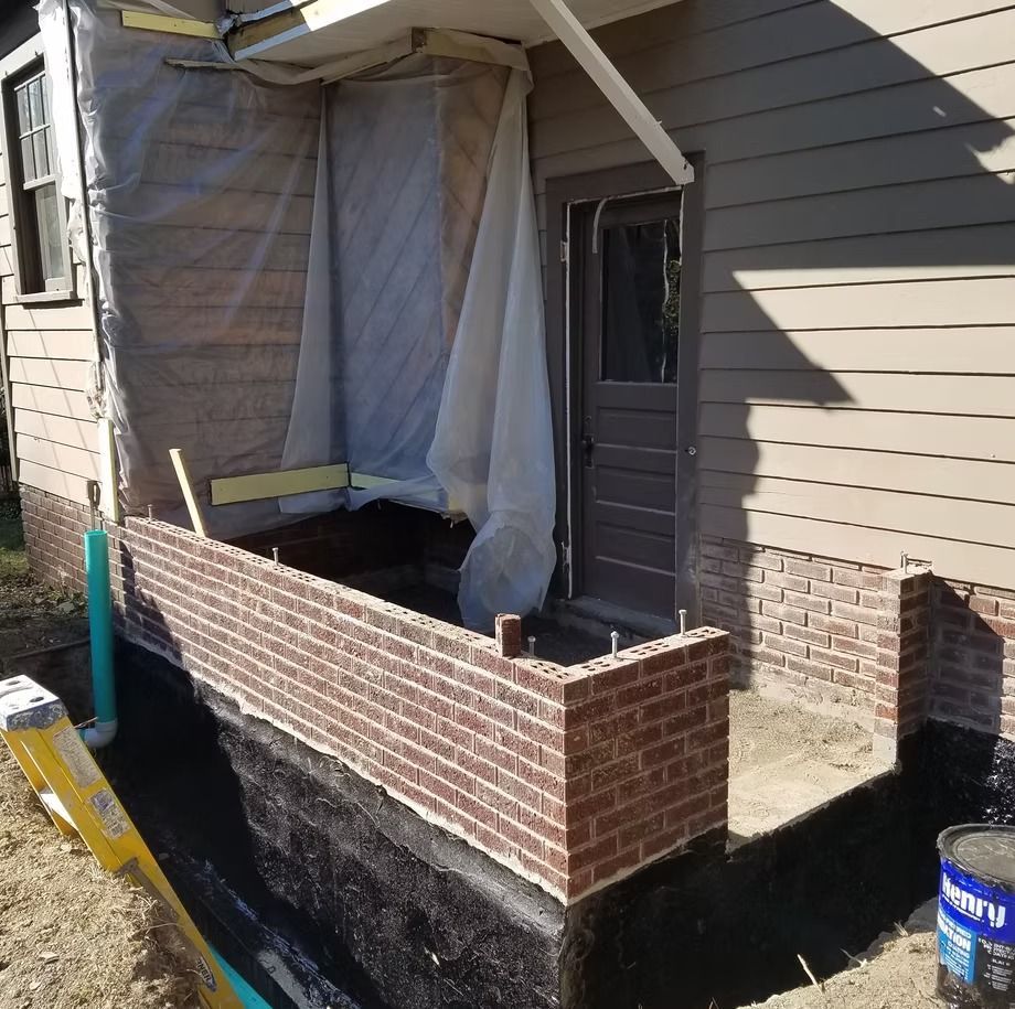 Partially built brick porch/entry with plastic sheeting and construction materials beside a house