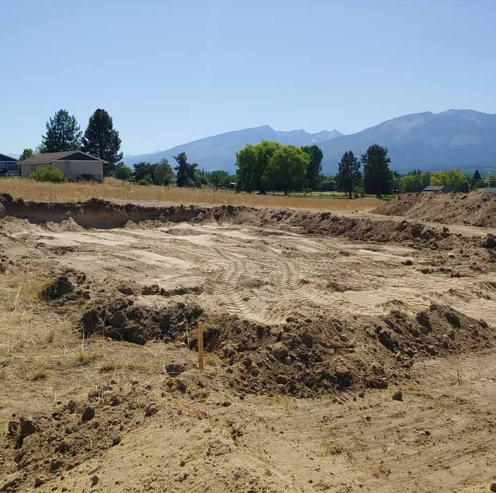 Dry dirt excavation site in a field with mountains and trees in the background.
