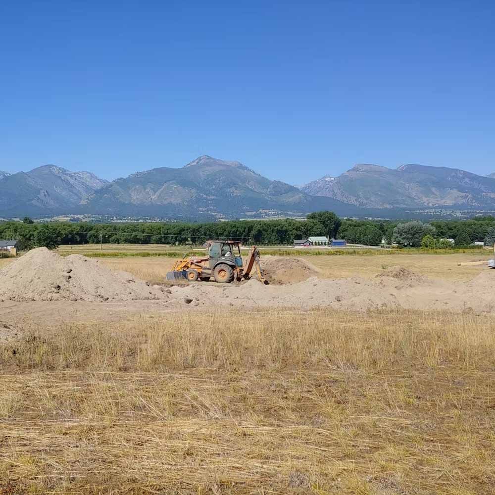 Bulldozer working on a dirt field with mountains and blue sky in the background