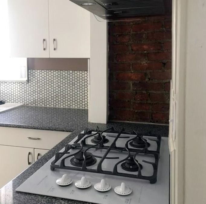 Small kitchen corner with a gas stove, white cabinets, and exposed brick wall.