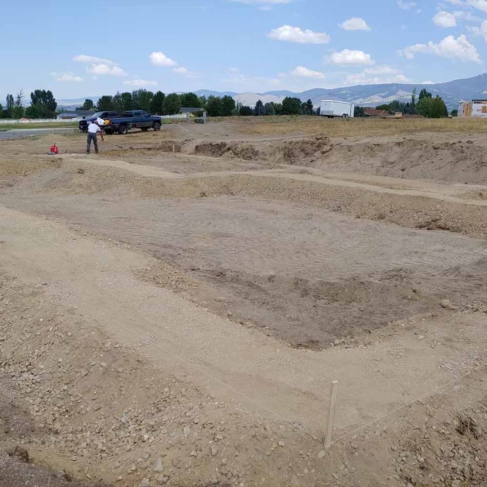 Excavated dirt lot with trenches, a parked pickup truck, and two people under a blue sky