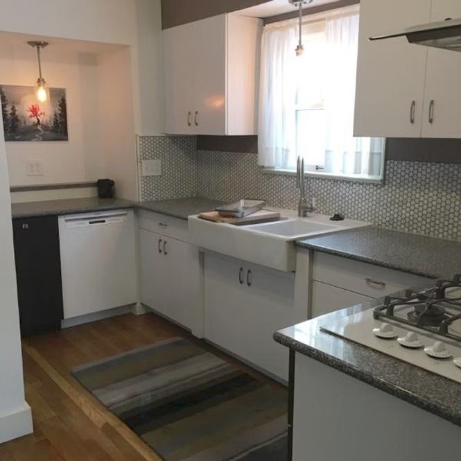 Modern kitchen with white cabinets, gray countertops, mosaic backsplash, and a window over the sink