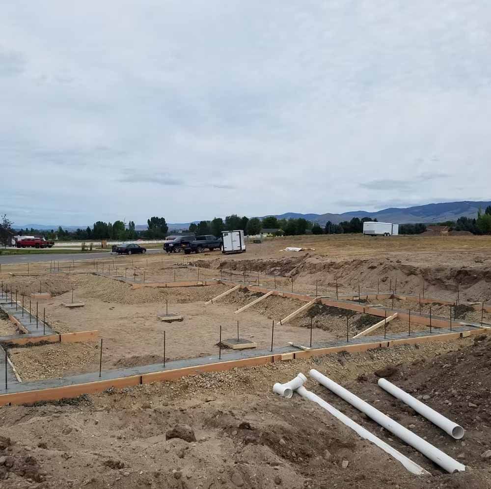 Construction site with excavated ground, rebar, pipes, and a cloudy sky background