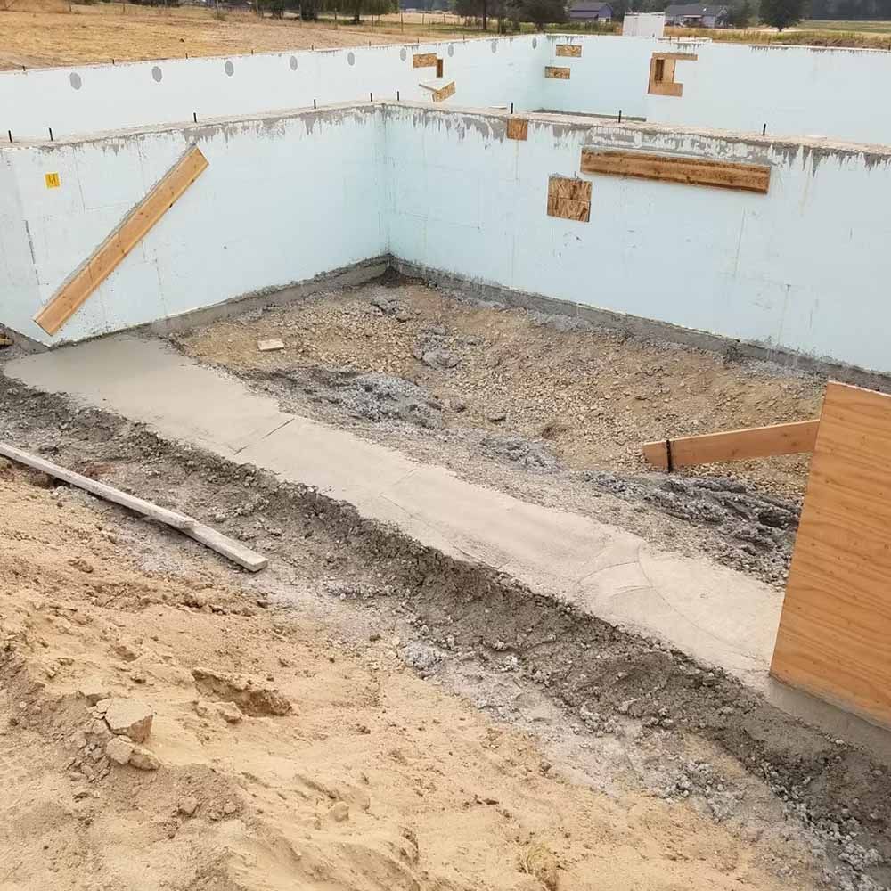 Construction site foundation with concrete walls, sandy floor, and wooden supports, viewed from an excavation pit
