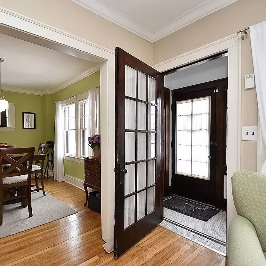 Bright foyer with open glass door, hardwood floors, and a dining room visible through a wide doorway