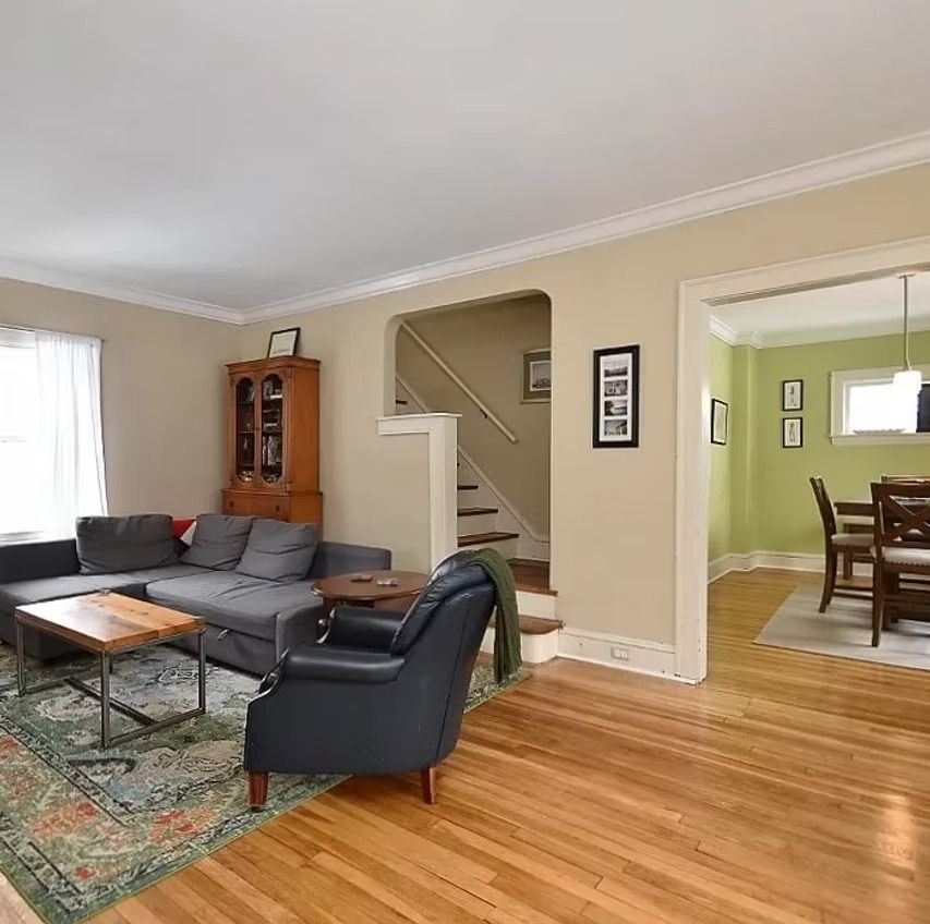 Living room with gray sectional, black chair, wood floor, staircase, and dining room visible through doorway