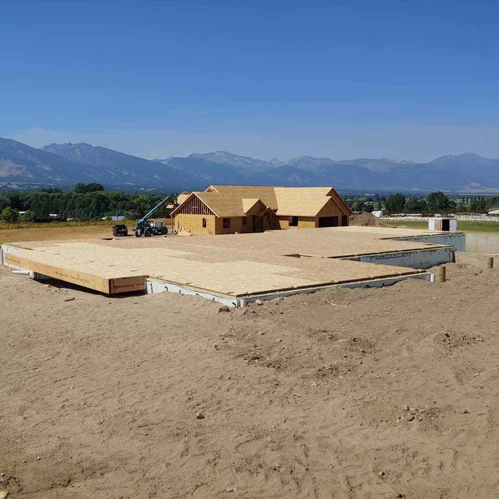 Wooden house under construction on a dirt lot with mountains in the background