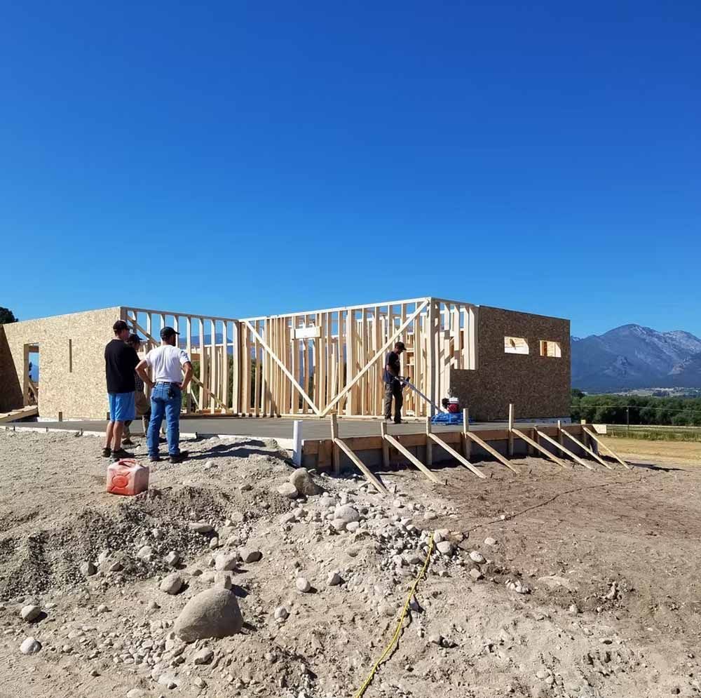 Workers framing a house under construction on a dirt lot with mountains in the background