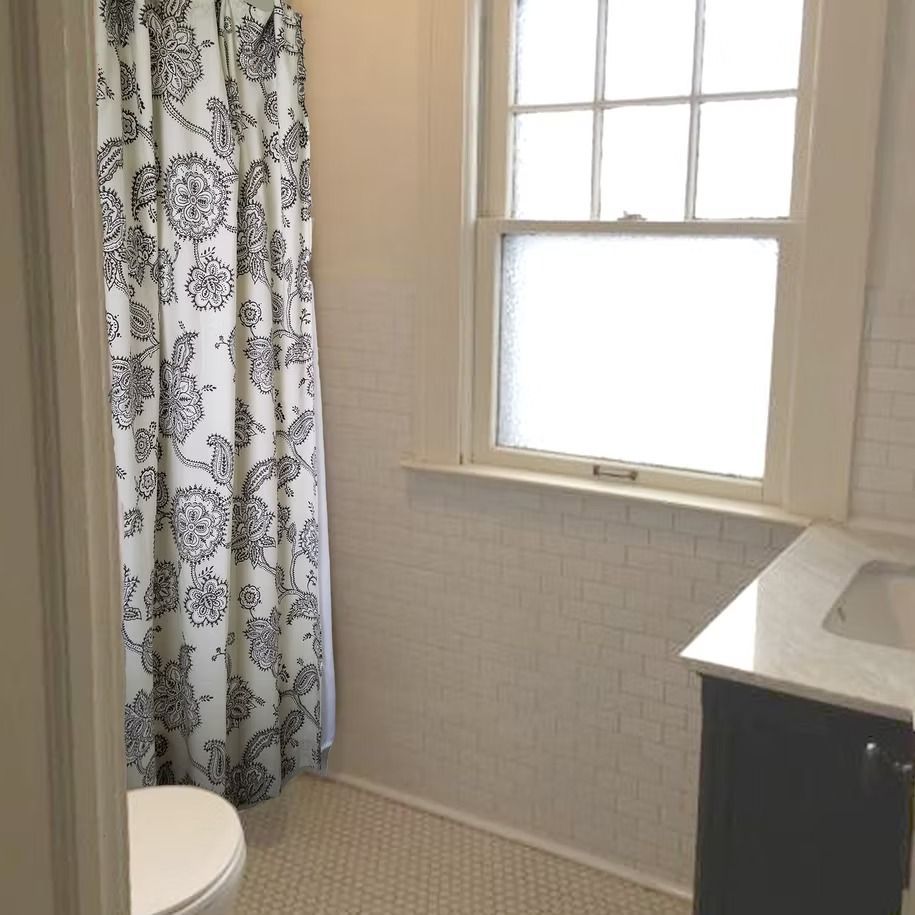 Small bathroom with shower curtain, toilet, window, and sink vanity.