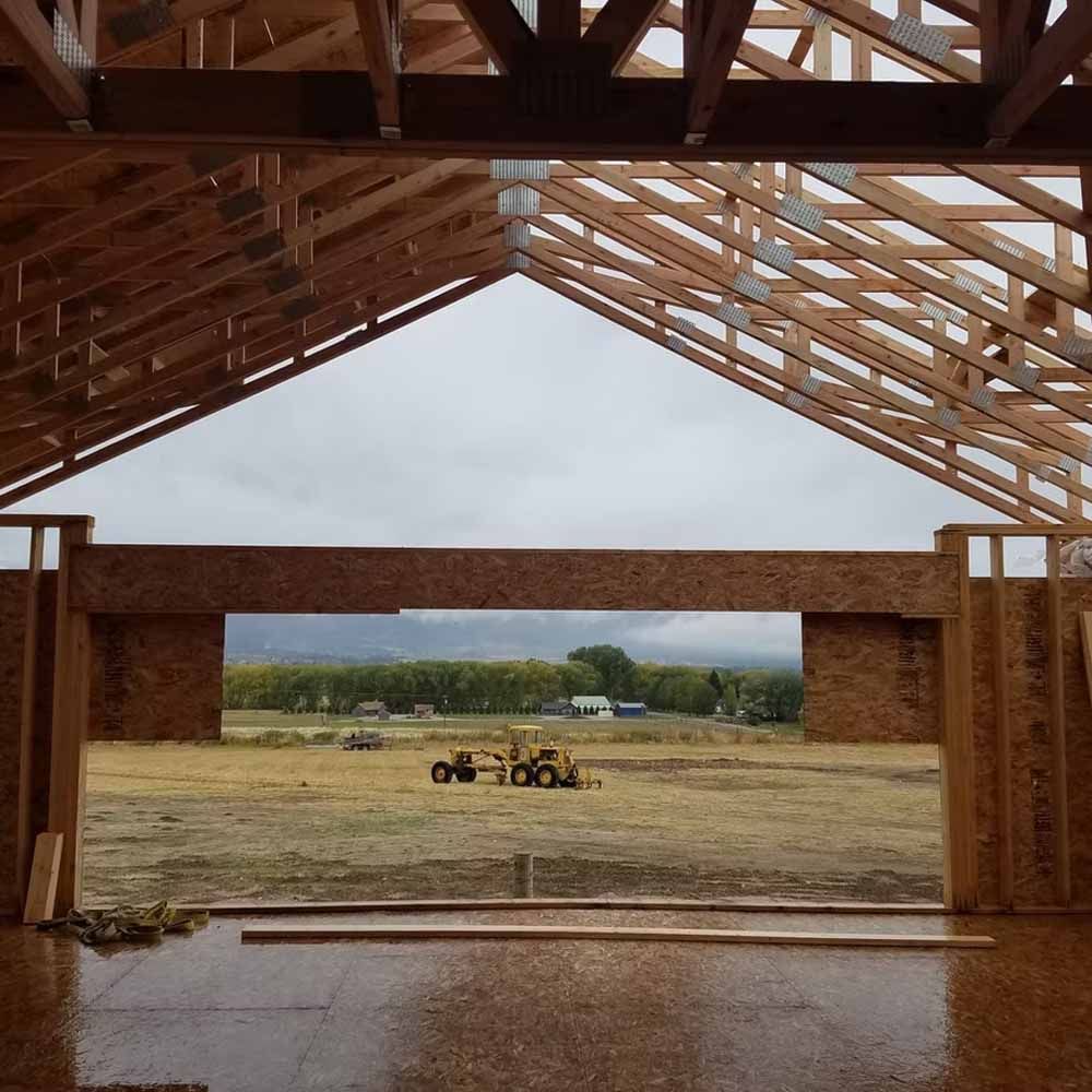 Interior of a wooden barn under construction, with a tractor on a field visible through the open front.