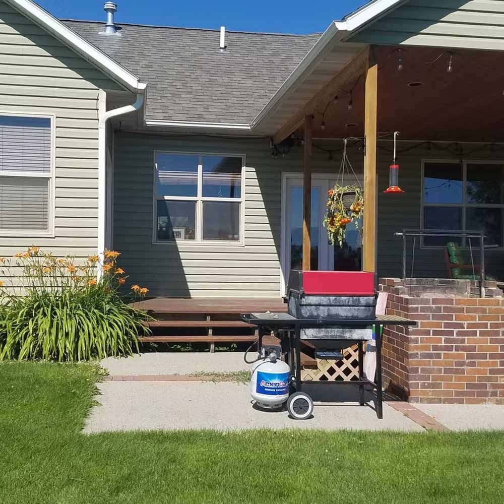 Front porch with brick half wall, red chair, grill, and potted flowers outside a beige house