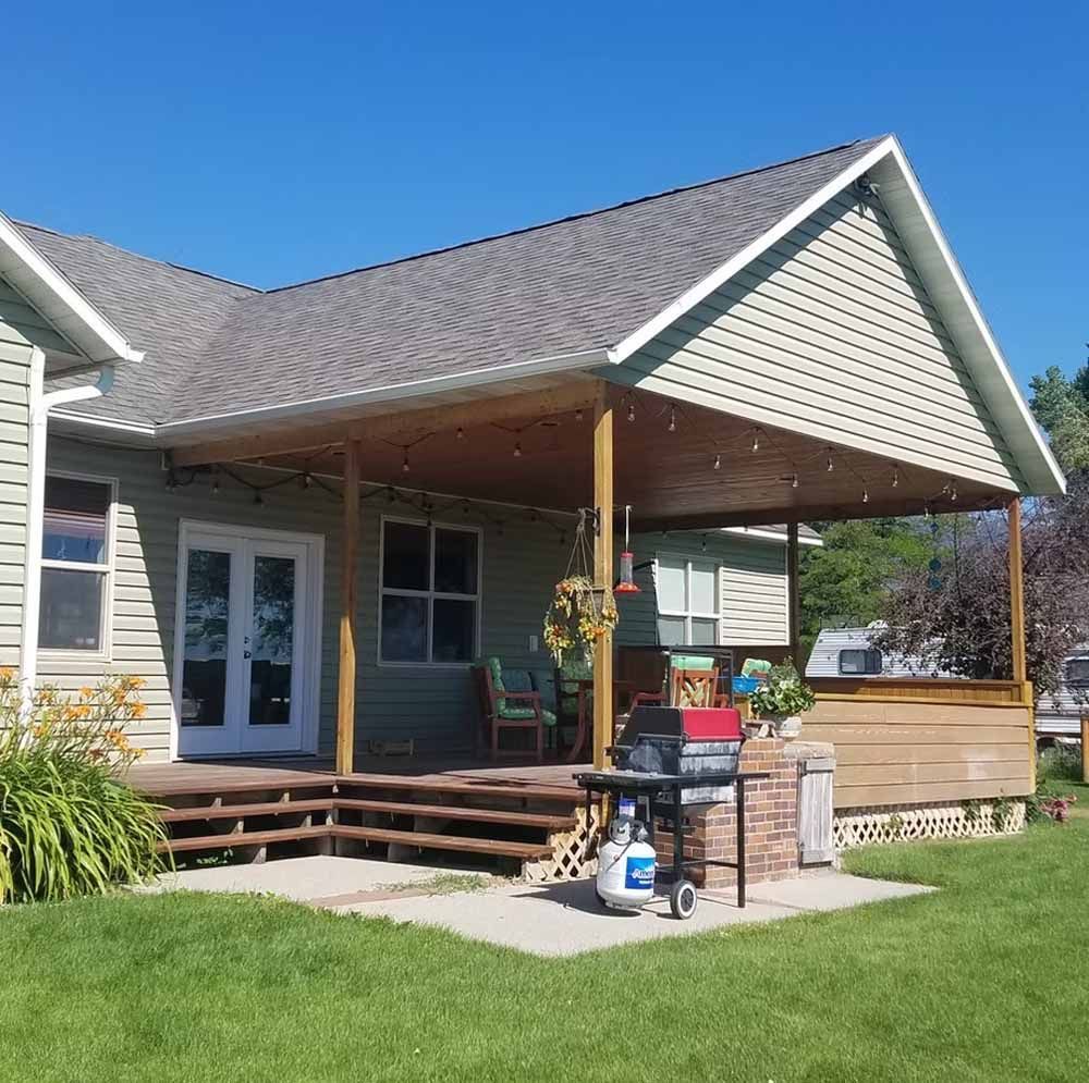 House exterior with covered porch, wooden steps, and a grassy yard on a sunny day