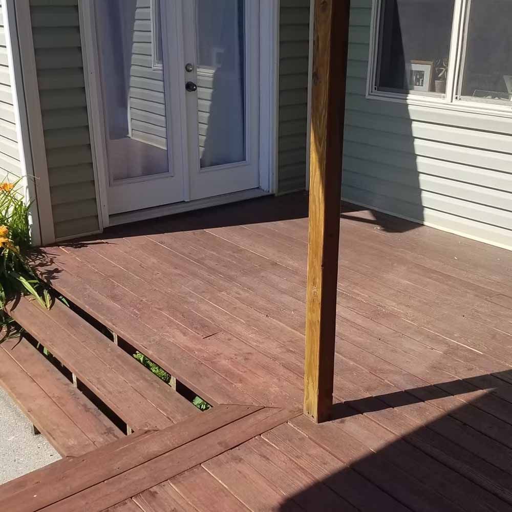 Wooden porch deck with a vertical support post and glass doors beside a house exterior.