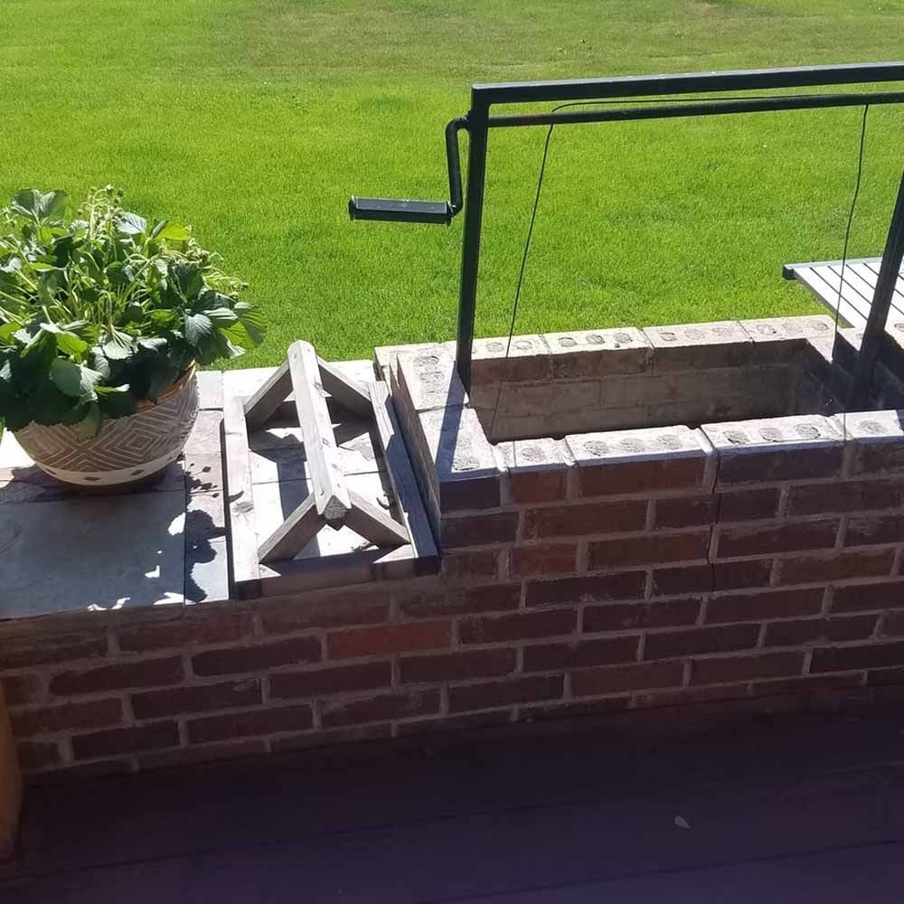 Brick patio with stacked bricks, potted plant, and black metal railing beside a green lawn