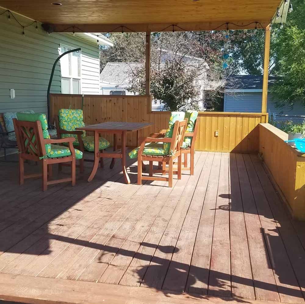Covered wooden deck with outdoor table and chairs in a sunny backyard
