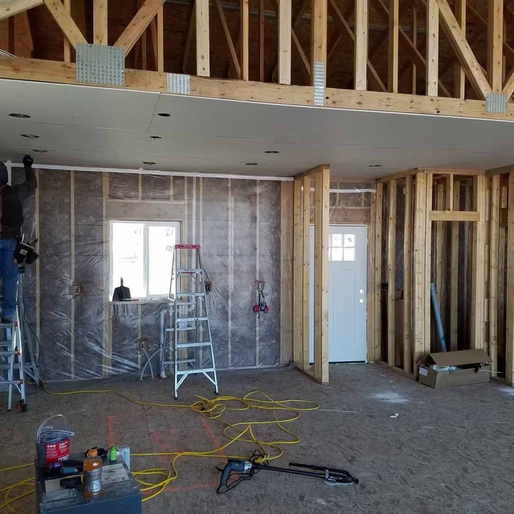 Interior of a house under construction with exposed framing, drywall, ladders, and tools on the floor