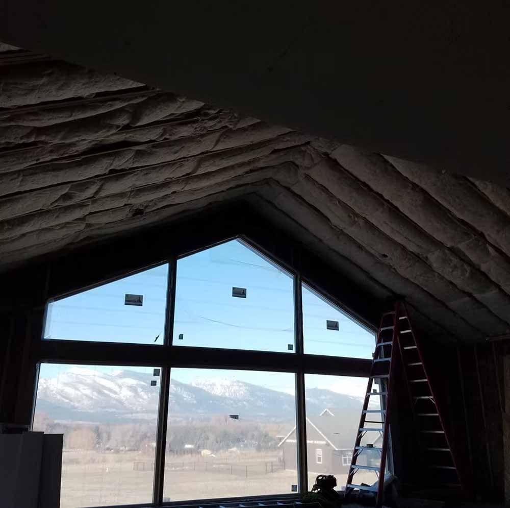 Interior view through a large triangular window framing snowy mountains, with a ladder at right.
