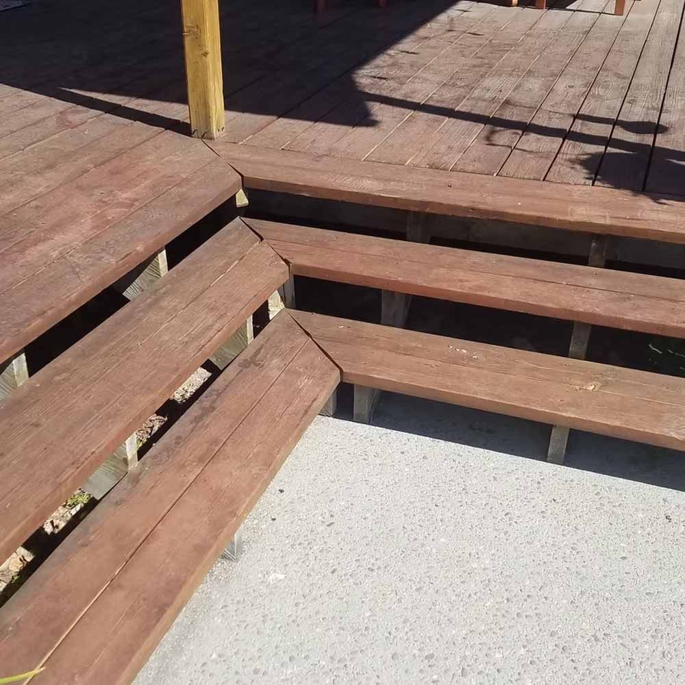 Wooden deck steps and railing around a concrete patio area in bright sunlight