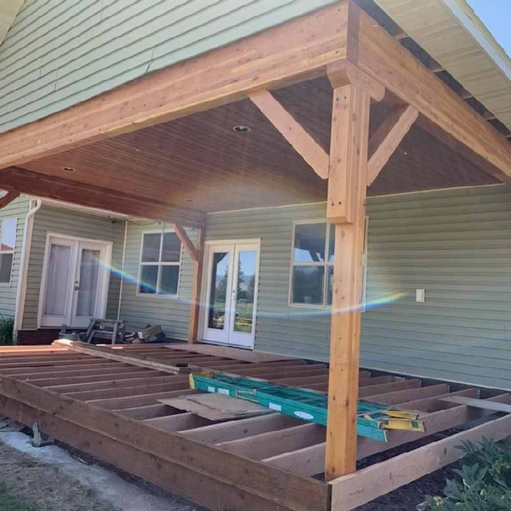Back porch under construction with wooden framing and roof posts beside a house