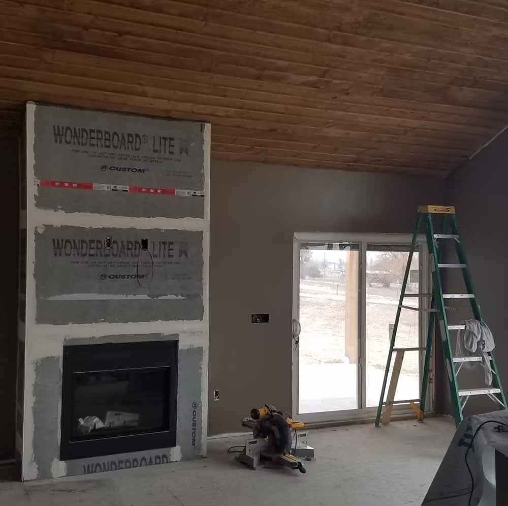 Living room under renovation with unfinished fireplace, wood ceiling, sliding door, and ladders by the wall