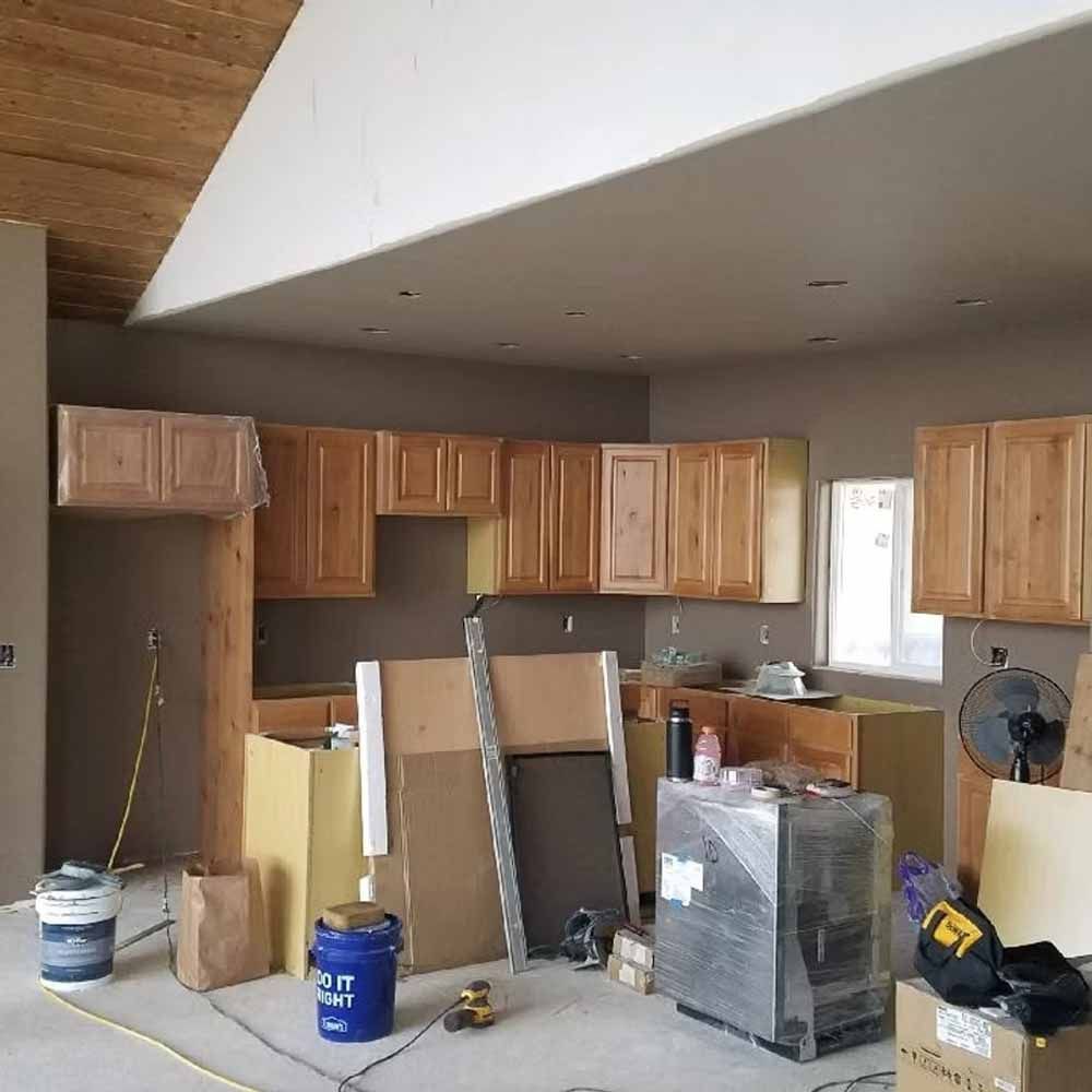 Kitchen under renovation with unfinished cabinets, drywall, and construction materials scattered on the floor