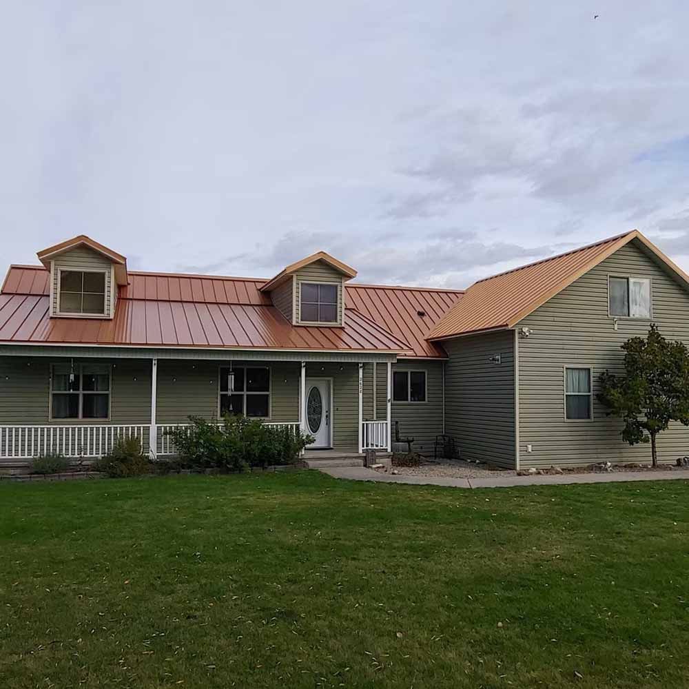 Single-story house with a red metal roof, white porch, and green siding on a grassy lawn.