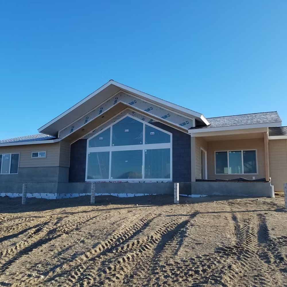New house exterior with large front windows and dirt driveway under a clear blue sky