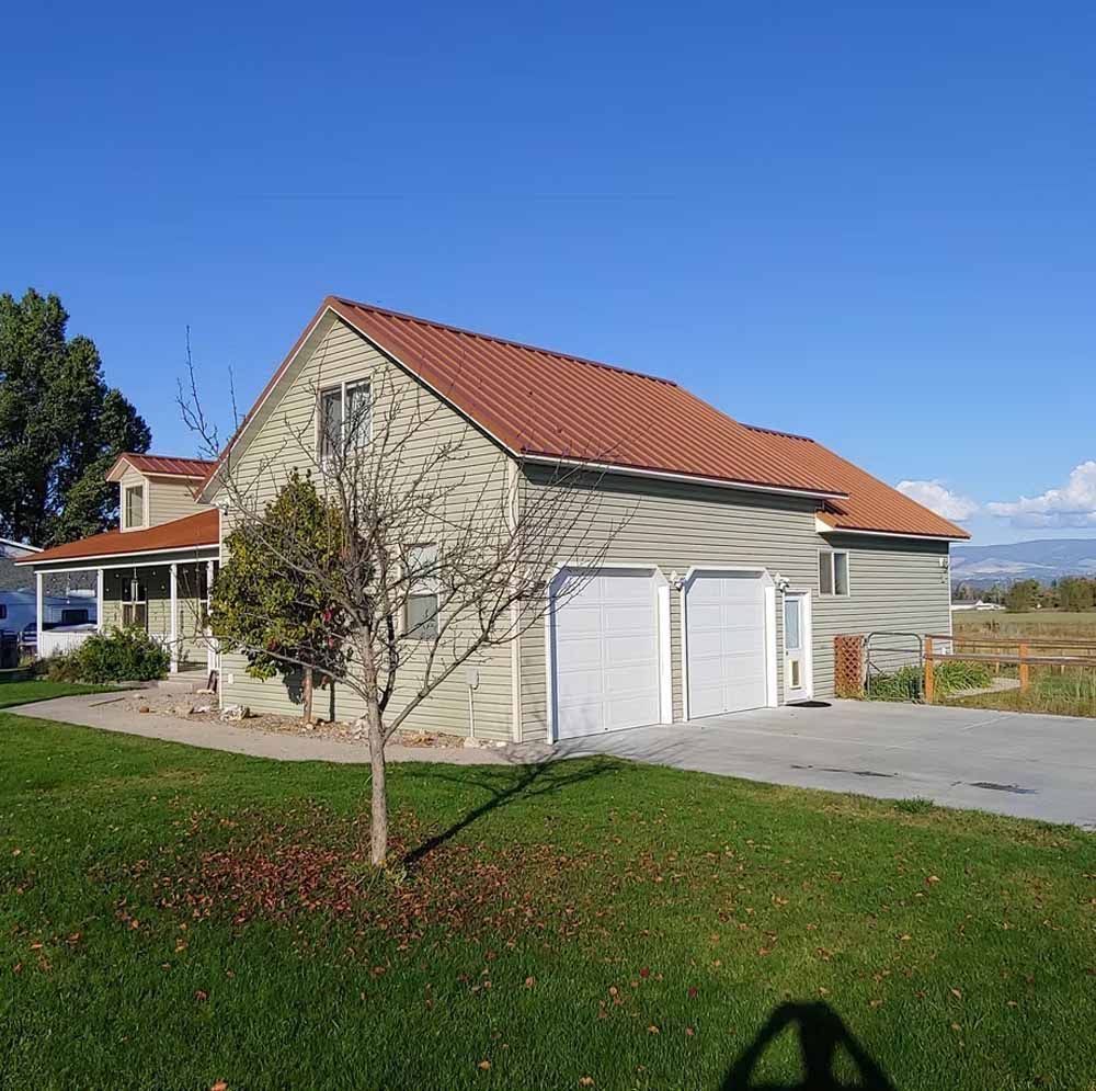 Suburban house with red roof, white garage doors, and a small tree in front under a clear blue sky
