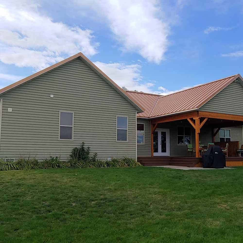 Single-story green house with red roof and covered porch on a grassy lawn under a cloudy sky