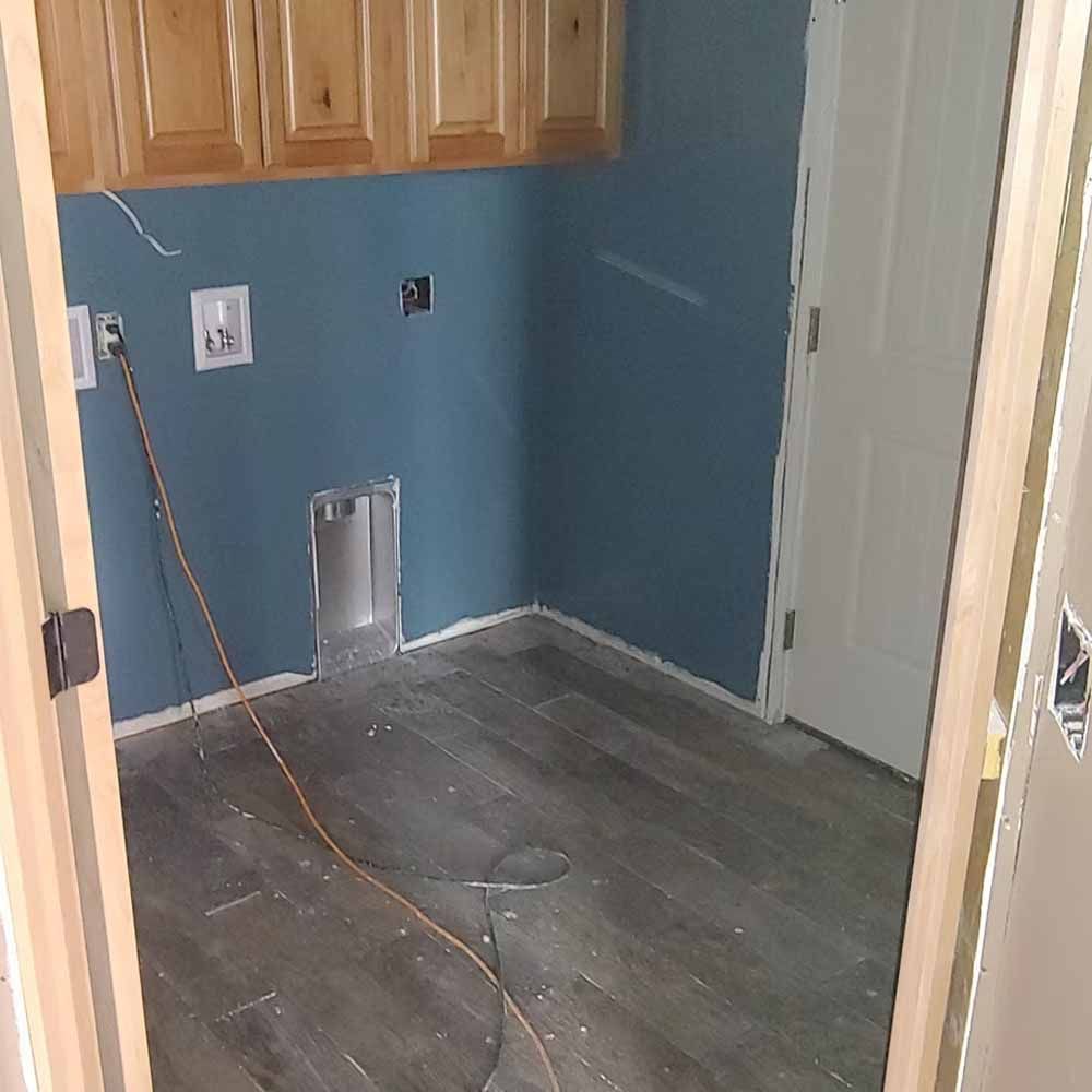 Empty kitchen corner with blue walls, wood cabinets, and a dishwasher opening under construction