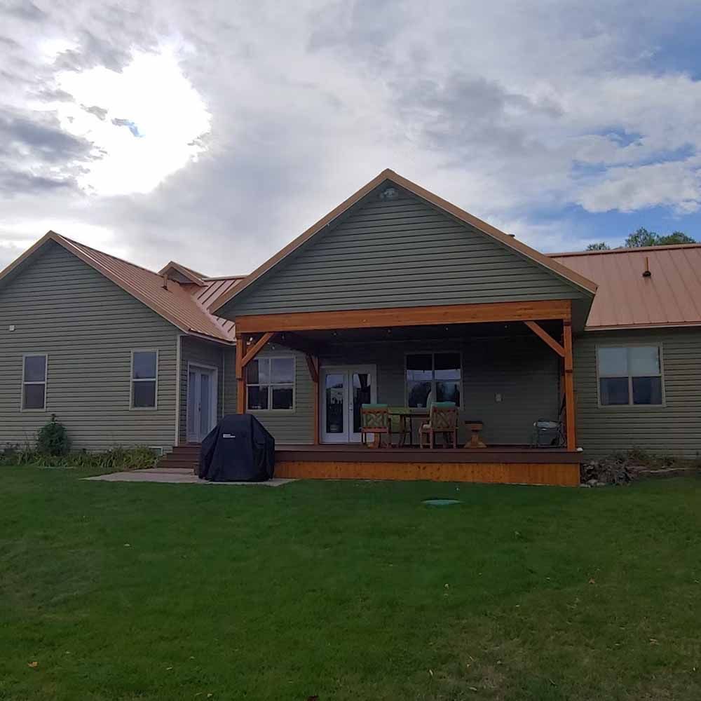 Suburban house with covered back porch, green lawn, and a grill under cloudy skies