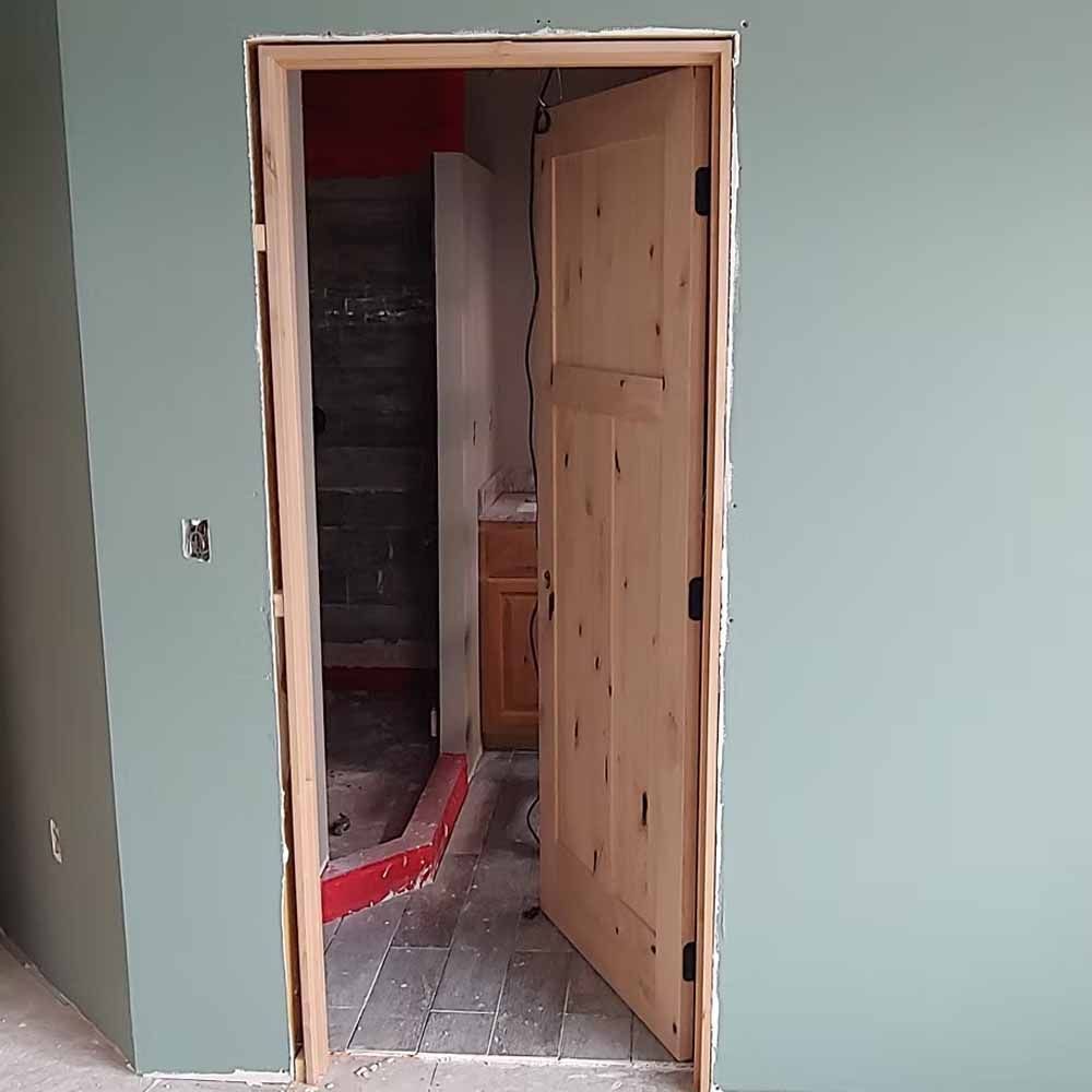 Partially open unfinished wooden door in a framed doorway of a room under construction