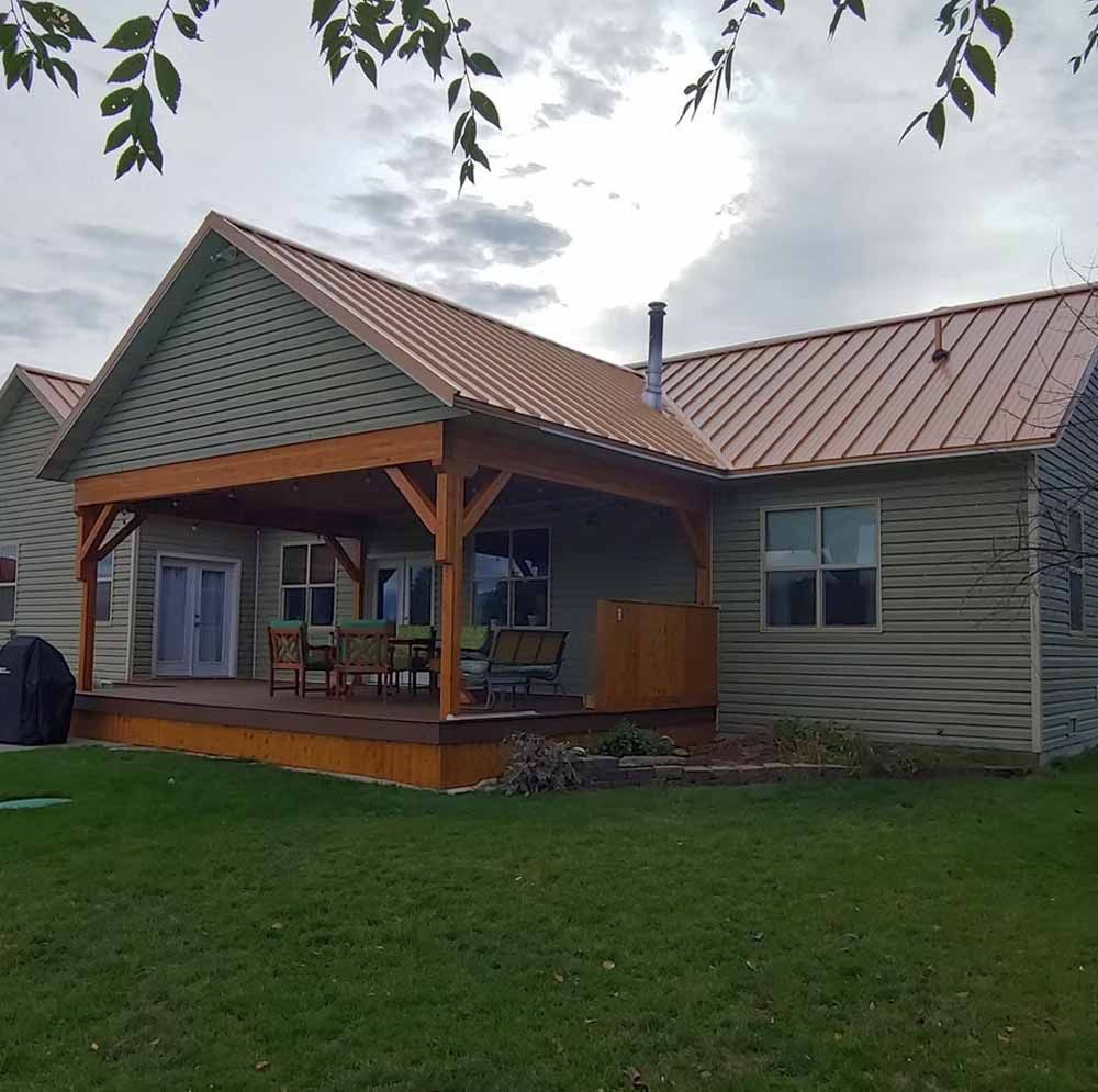 Single-story house with a covered porch, green siding, and a red metal roof on a lawn