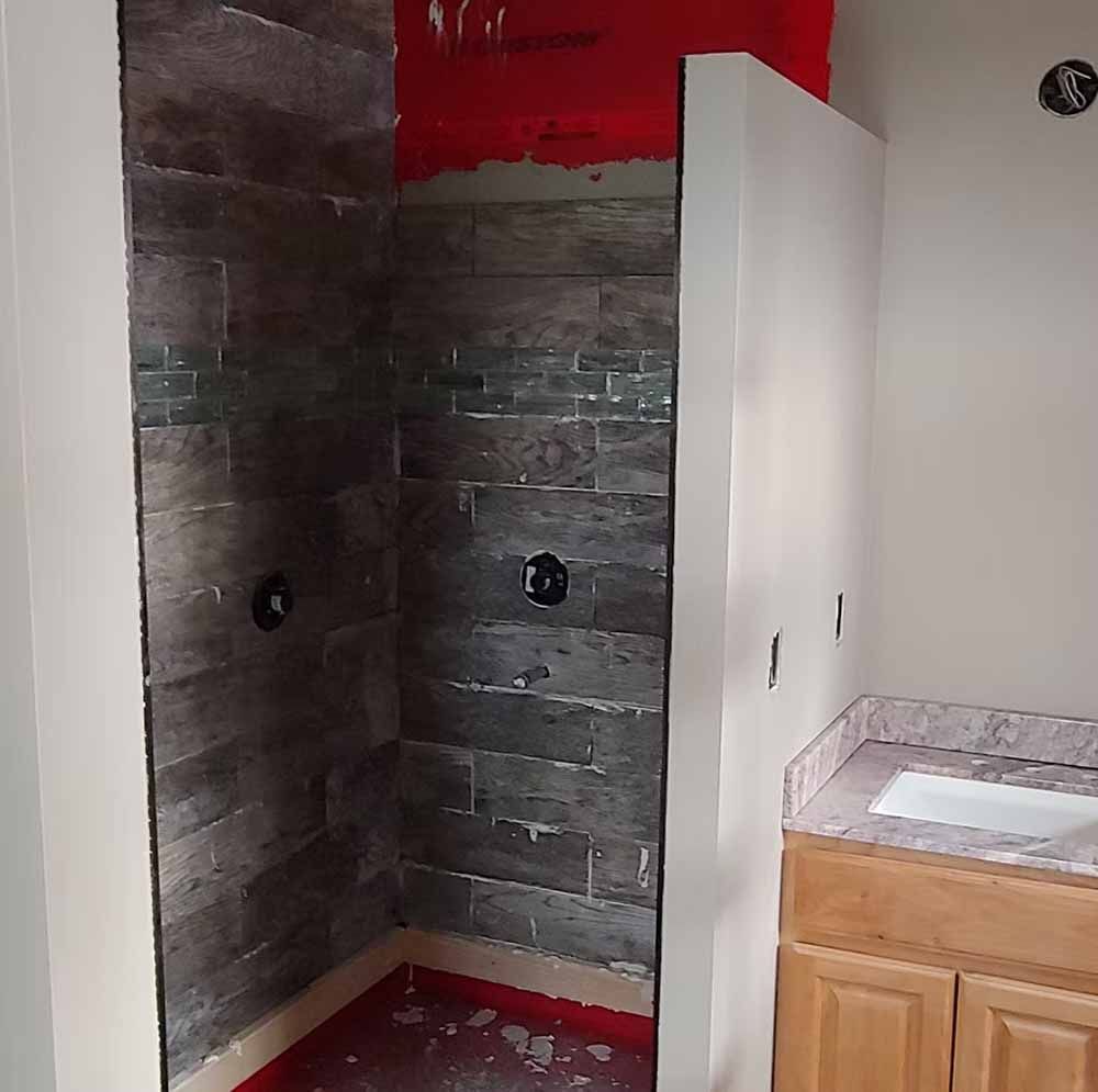 Small tiled shower stall under renovation beside a white cabinet and sink in a bathroom.
