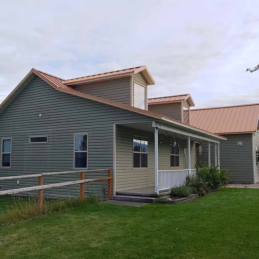 Exterior of a green house with a covered porch and red metal roof beside a grassy yard