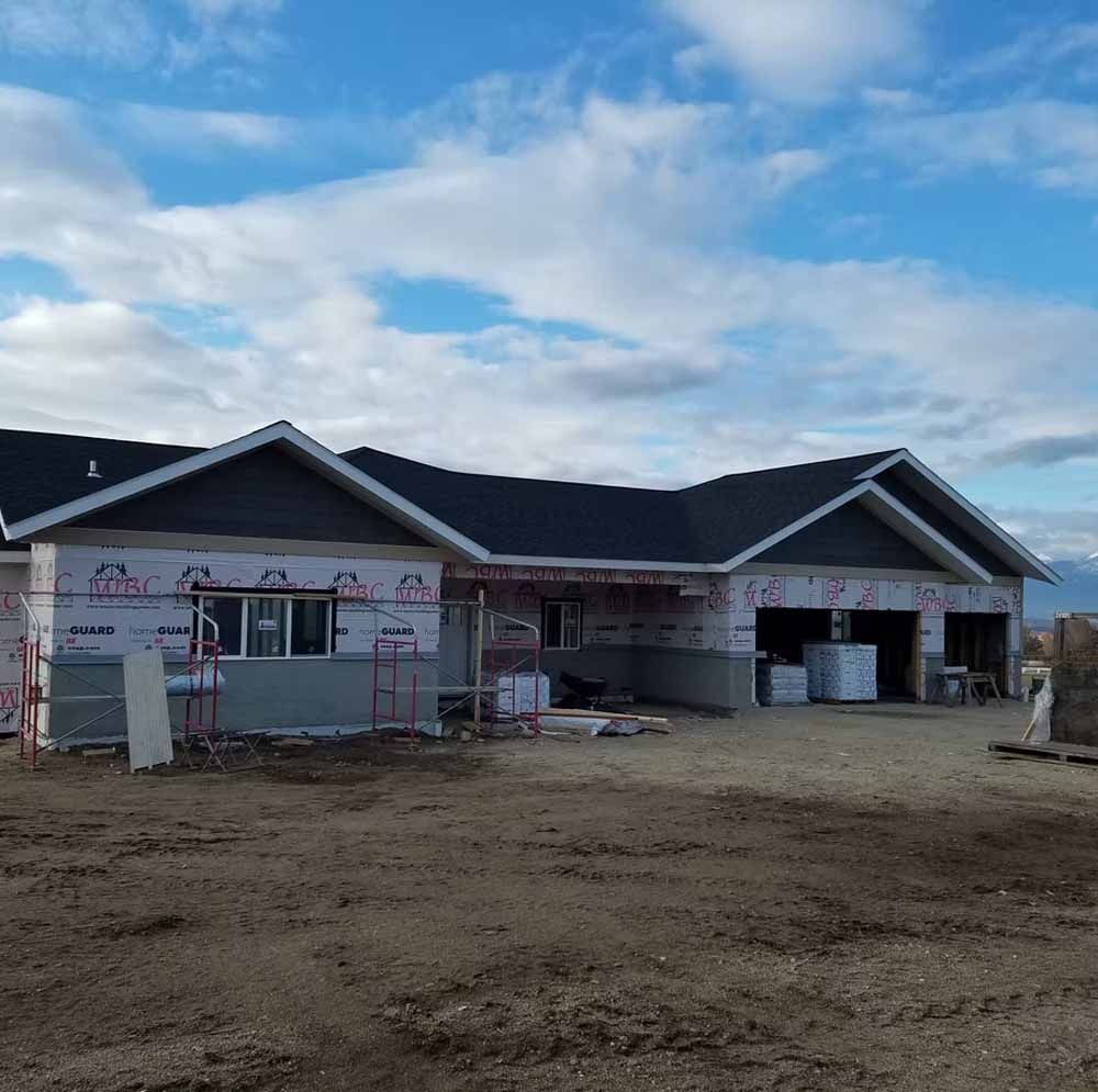 New house under construction with gray roof, unfinished exterior, and dirt foreground under a cloudy sky