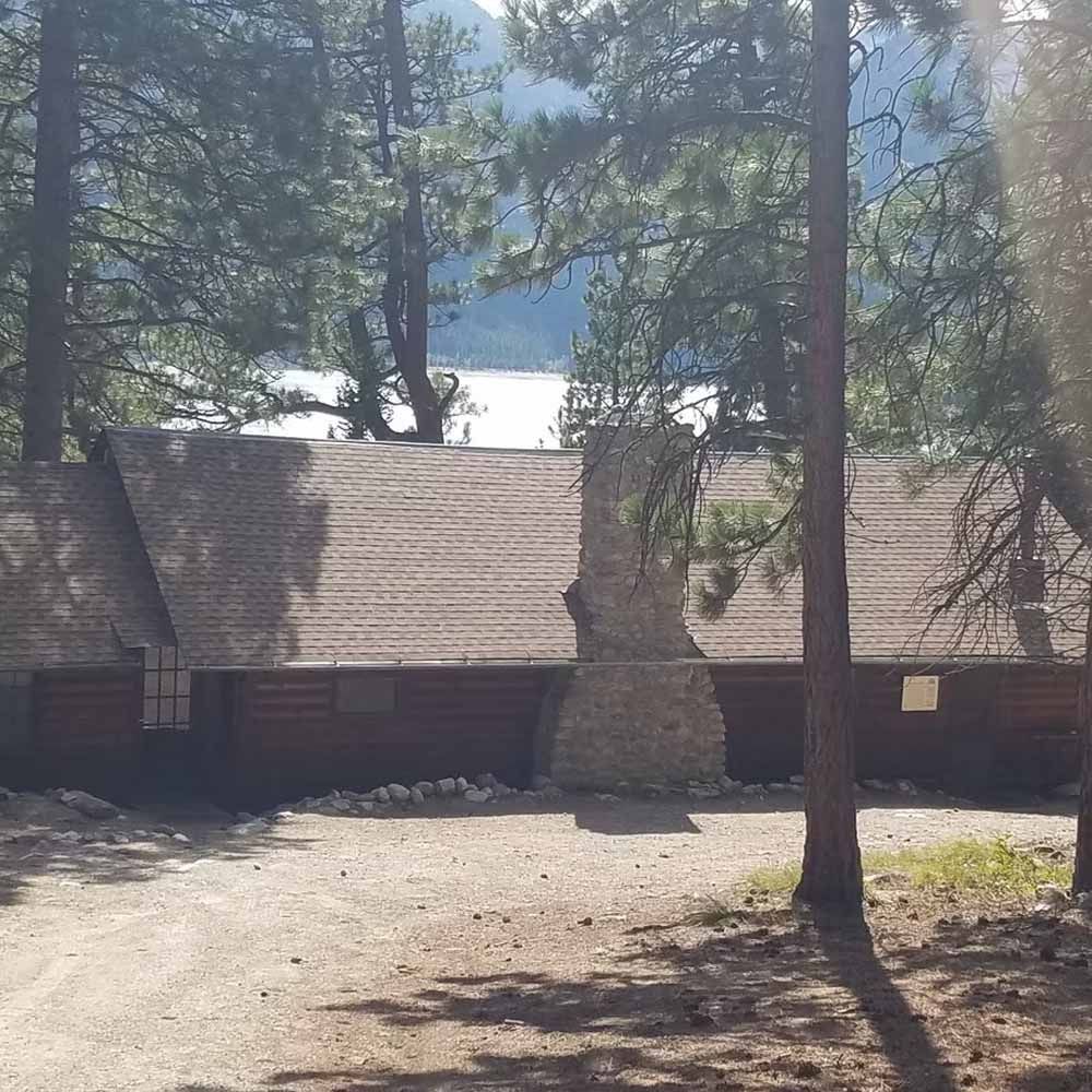 Wooden cabins among pine trees with a lake and mountains in the background