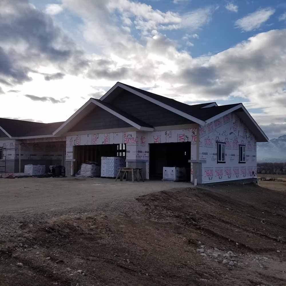 Partially built suburban house with white wrap and open garage under a cloudy sky