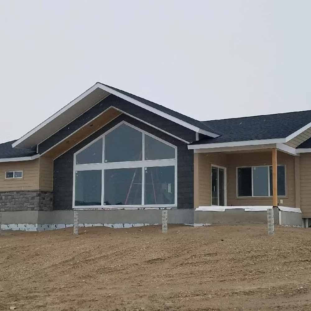 New home exterior with large front windows, dark roof, and unfinished dirt yard