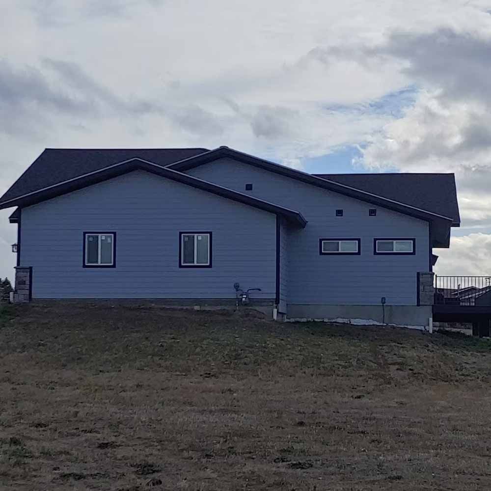 Gray house with dark roof on a grassy lot under a cloudy sky