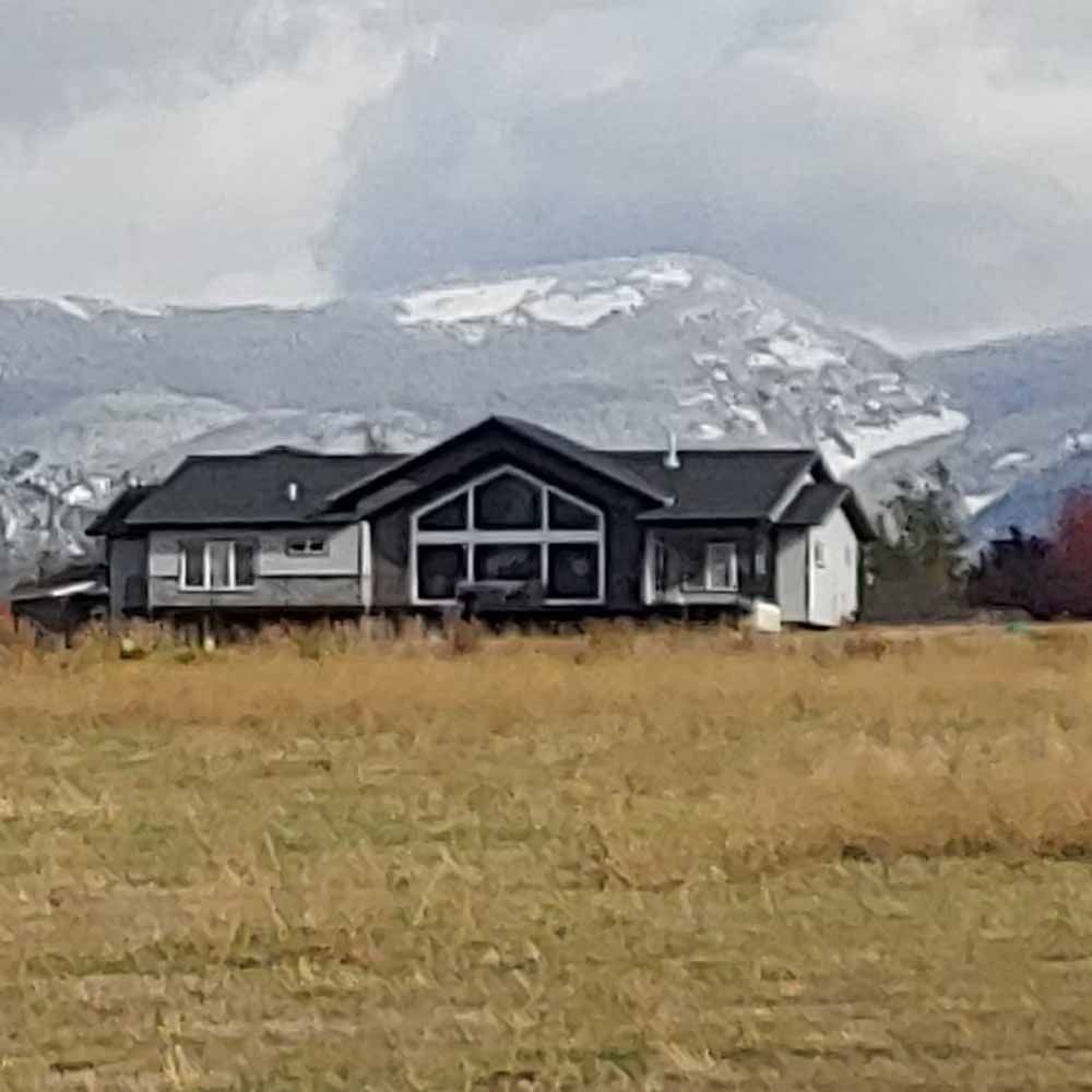 Dark house in a grassy field with snowy mountains and cloudy sky in the background